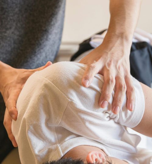 Crop anonymous medical specialist rubbing shoulders of male client lying on couch in medical salon