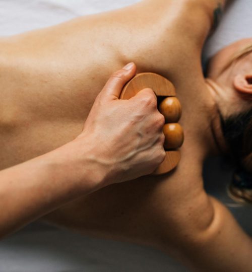 Woman receiving a relaxing back massage with a wooden tool in an indoor, serene setting.